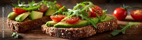 Two slices of multigrain toast topped with avocado, cherry tomatoes, and fresh greens rest on a wooden surface