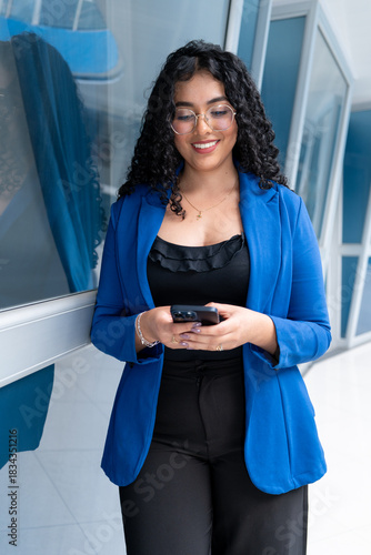 Young and beautiful businesswoman with curly hair uses her phone while standing. vertical