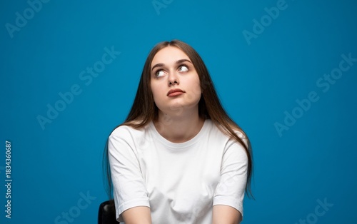 Konstfotografi Woman rolling eyes upward in boredom on blue background, unimpressed facial expr