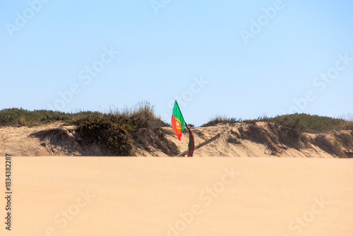 Portuguese flag behind coastal dune against bright blue sky Portugal, Ovar – Furadouro, 10.10.2025