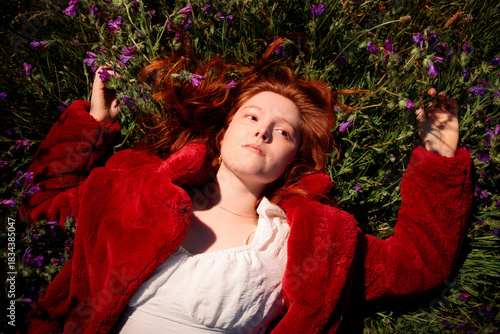 Young red haired woman lying in wildflowers under warm afternoon light