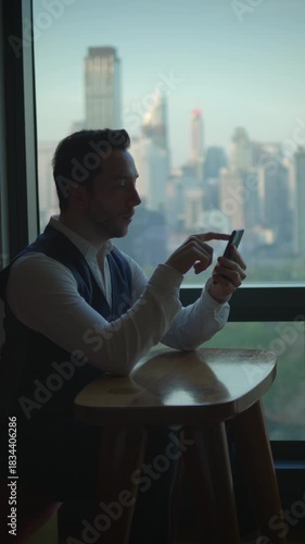 man works remotely, man sitting at table concentrating on his phone with city views passing outside