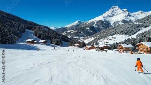 Child skier on snowy mountain slope with chalets and pine trees on a sunny day