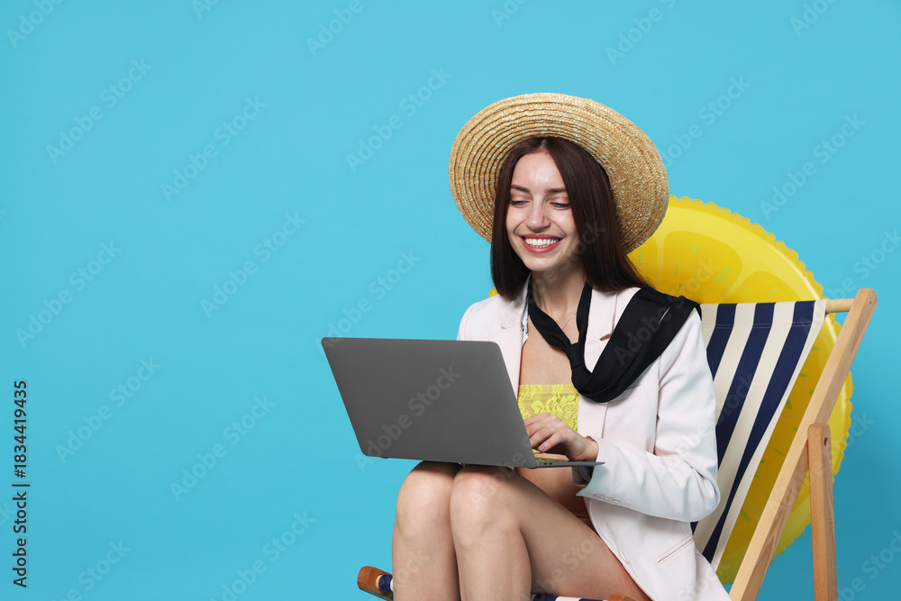 Fototapeta premium Businesswoman with laptop in deck chair and inflatable ring on light blue background, space for text