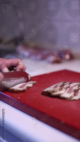 a man's hands cutting bacon on a red cutting board in his home kitchen