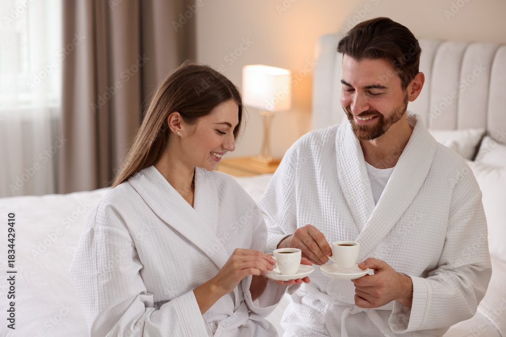 Obraz premium Happy couple in bathrobes with morning coffee on bed indoors