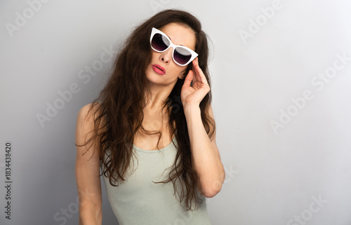 Portrait of elegant woman posing white sunglasses and fashion top on grey wall background with empty copy space for text. Front view face emotion sexy summer studio portrait