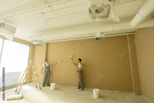 Foto Two workers painting a brown wall in an office space during daylight hours