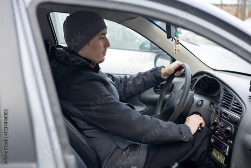 A man inside a car, the driver behind the wheel in cold weather