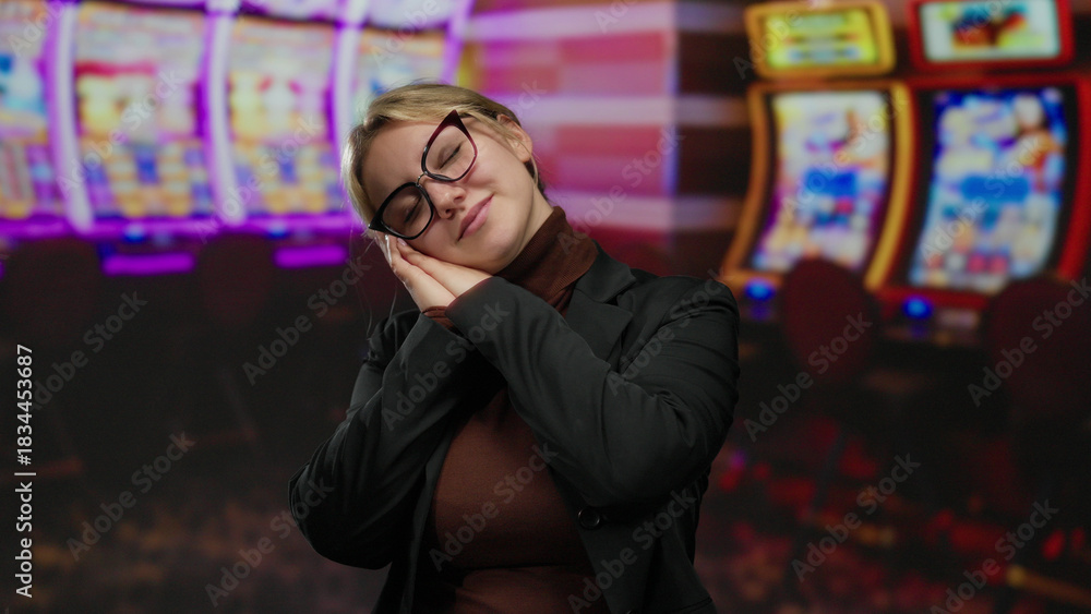 Obraz premium Woman resting in casino with slot machines in the background, showing a relaxed posture amidst flashing lights and vibrant screens.