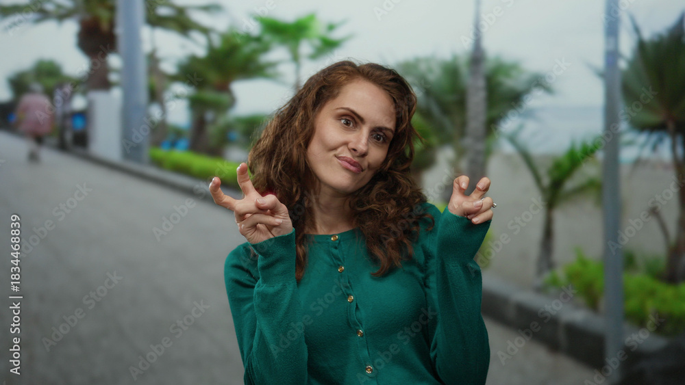 © Krakenimages.com - Woman making playful gestures near palm-lined promenade by the beach on a cloudy seaside day.