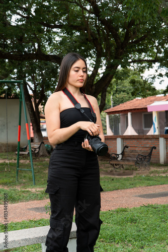 Girl with black clothes holding a reflex camera at the park.