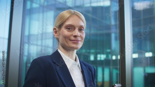 Confident blonde Caucasian businesswoman holding smartphone. Getting briefly distracted and making eye contact with camera. Pausing in the middle of a task. Looking directly and smiling.