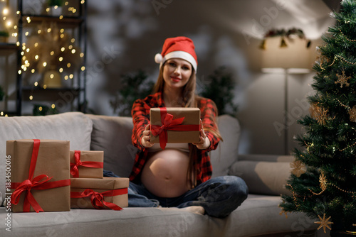 A pregnant woman wearing a Santa hat offers a wrapped gift during the Christmas season