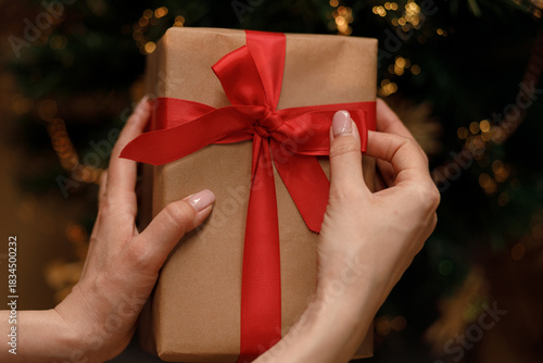 Hands carefully tie a festive red ribbon around a wrapped present, perfect for any special occasion