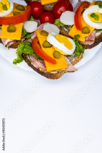 Healthy sandwiches made from whole wheat bread with egg, pickles, tomato, and chives arranged on a white plate. The plate with the sandwiches is placed against a white background.