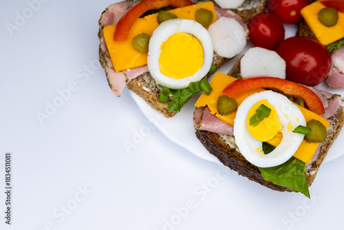 Healthy sandwiches made from whole wheat bread with egg, pickles, tomato, and chives arranged on a white plate. The plate with the sandwiches is placed against a white background.