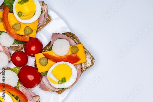 Healthy sandwiches made from whole wheat bread with egg, pickles, tomato, and chives arranged on a white plate. The plate with the sandwiches is placed against a white background.