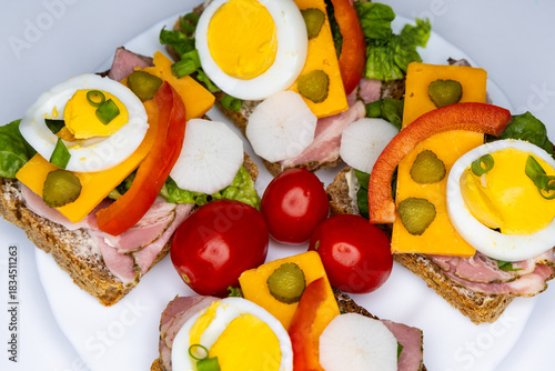 Healthy sandwiches made from whole wheat bread with egg, pickles, tomato, and chives arranged on a white plate. The plate with the sandwiches is placed against a white background.