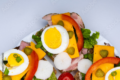 Healthy sandwiches made from whole wheat bread with egg, pickles, tomato, and chives arranged on a white plate. The plate with the sandwiches is placed against a white background.