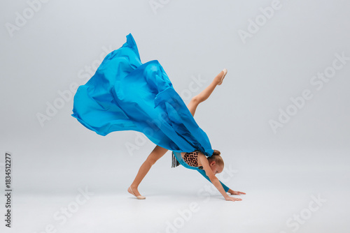 Dancer in sport leotard doing Split. Cheerleader dancing with flying blue cloth fabric. Graceful ballerina dancing on grey studio background. Child, artist, movement, action and motion concept