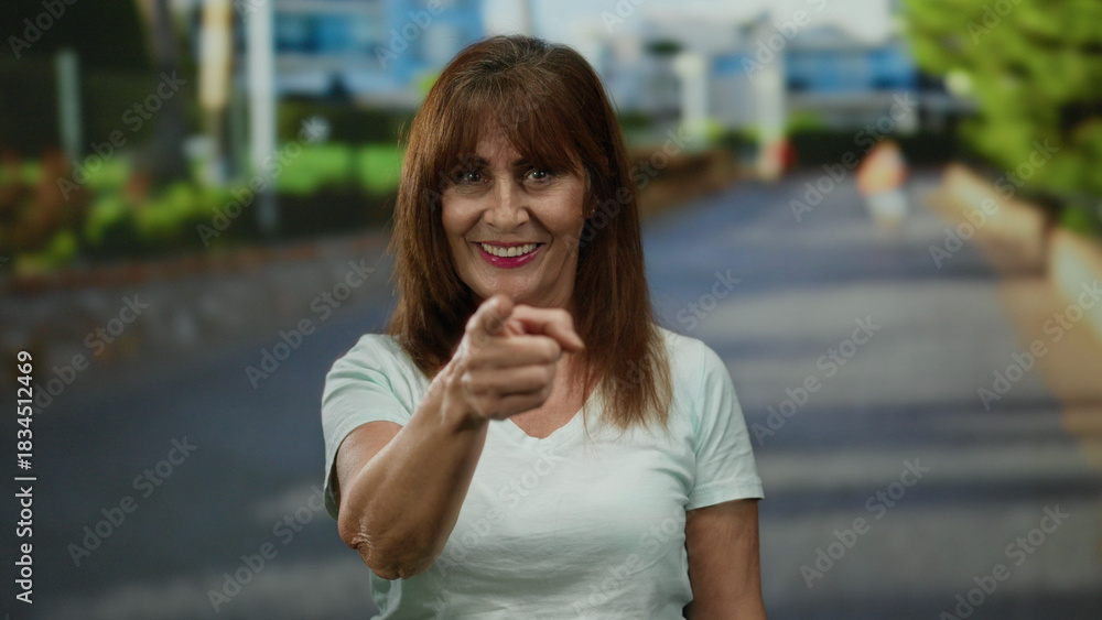 Fototapeta premium Woman smiling and pointing energetically in an urban outdoor city street, capturing a lively and engaging moment with a vibrant expression under sunny skies.