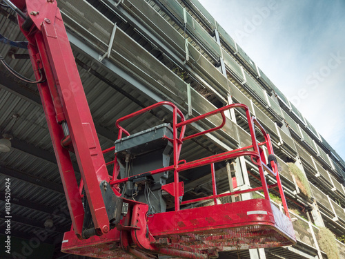Red aerial work platform extending upwards for maintenance work on a modern building