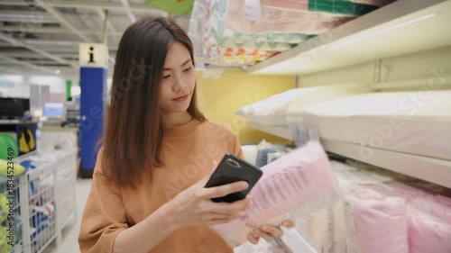 Shopping concepts of 4k Resolution. An Asian woman is checking prices on her mobile phone while comparing blankets in a department store.