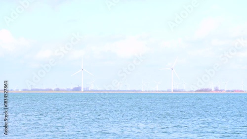 A row of wind turbines rises along the distant shoreline above calm water.