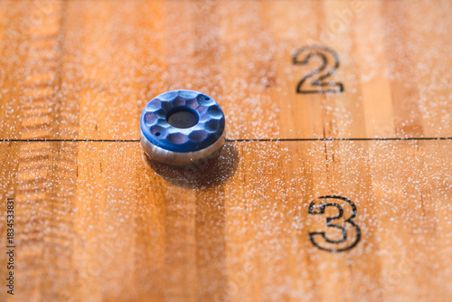 Blue shuffleboard puck on polished wooden scoring lane.