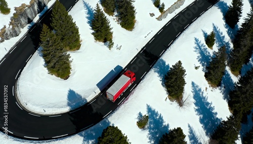 Aerial drone shot of red truck navigating dangerous winding switchback road in snowy Alps mountains