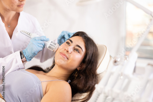 Young brunette girl having facial beauty procedure with ice hummer attachment of beauty machine