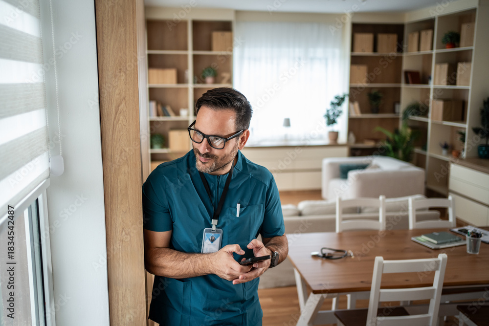 Fototapeta premium Male doctor using phone having a break at home