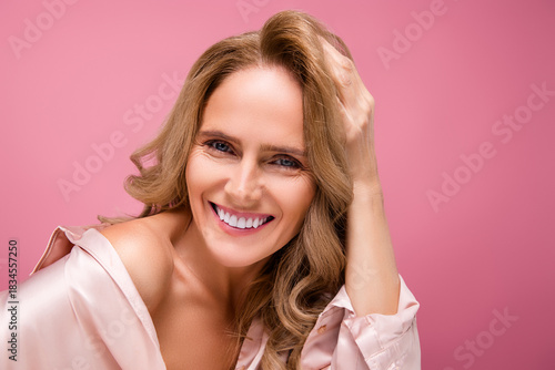 Beautiful mature woman smiling joyfully wearing pink sleepwear against a vibrant background