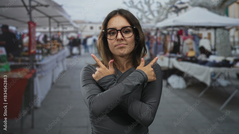 Fototapeta premium Woman wearing glasses arms crossed pointing fingers outward in street market stalls and souvenir booths; rejection.