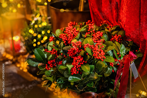 Christmas festive background with a bouquet of red holly berries and decorations with Christmas lights behind. New Year's Eve in golden lights. Winter holidays.