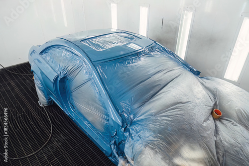 Photos Technician preparing a modern car for paint, carefully masking the body with specialized film inside the clean painting chamber