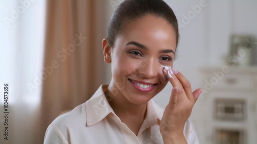 A beautiful young woman applying facial cream around her eye area, smiling towards the camera Stock Video