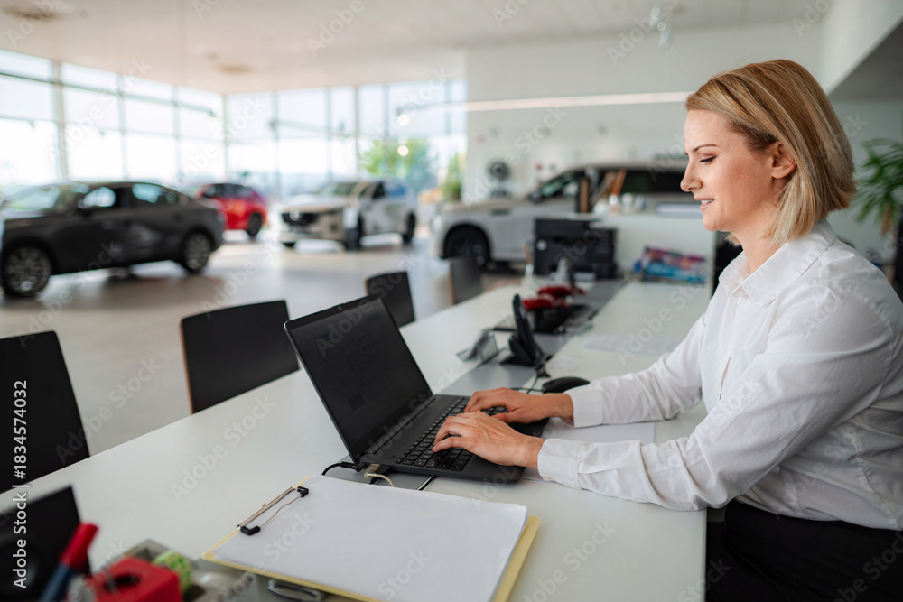 © Jelena - Car saleswoman typing on laptop in automotive dealership © Jelena - Car saleswoman typing on laptop in automotive dealership