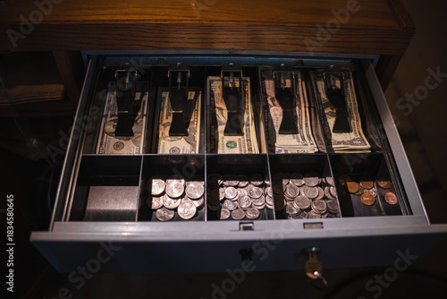 Open cash register drawer filled with organized US banknotes and assorted coins in compartments.