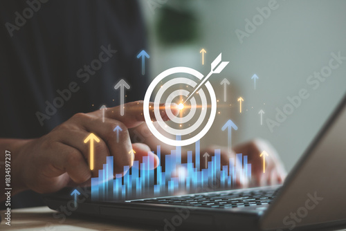 Person pointing digital target icon with virtual rising arrows and bar chart on laptop, symbolizing business growth, goal achievement, performance improvement, strategic success in modern analytics.