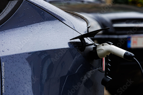 Electric car charging in rainy weather from rear view. Rear close-up of an electric car plugged into a charger with raindrops, symbol of clean energy and sustainable transport.