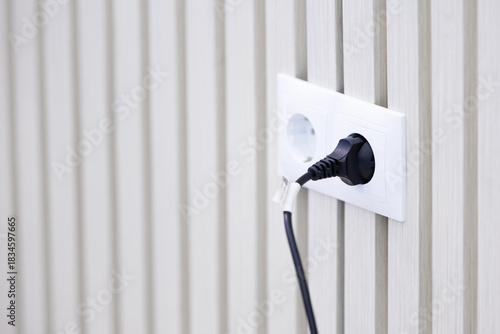 Modern power outlet with plugged cable on white textured wall. Minimalist scene of an electrical socket with a connected plug, symbol of energy, technology and everyday life.