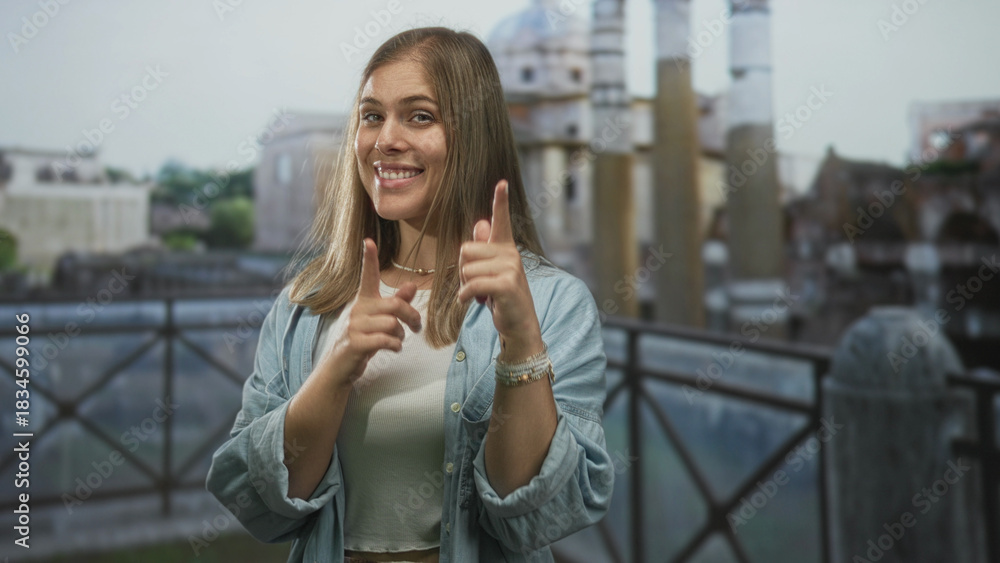 Fototapeta premium Woman points finger to camera beside historic stone building facade; invitation connection confidence.