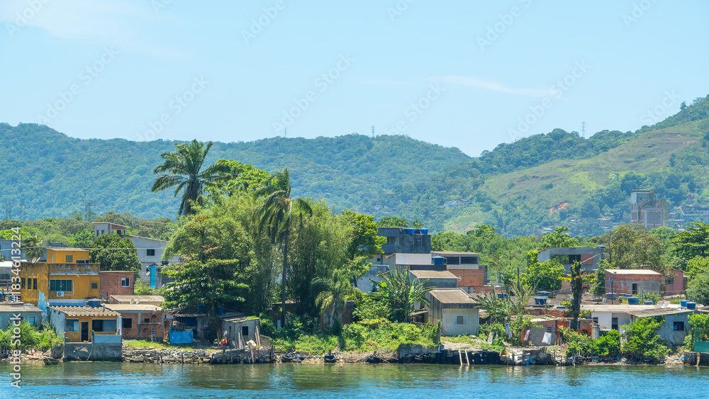 Fototapeta premium Vibrant waterfront community with modest houses and lush tropical vegetation, set against a backdrop of green, hilly mountains