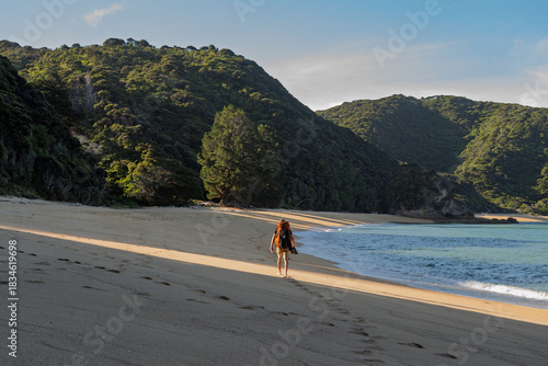 Barefoot hiker walking on golden sand beach at sunset, Abel Tasman, NZ