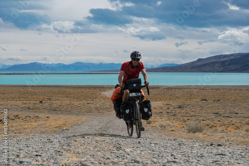 Cyclist riding gravel track in front of turquoise Lago Argentino, Patagonia
