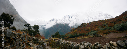 Snow-capped mountains loomed over a rocky path in a valley during the cloudy afternoon