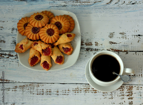Azerbaijani crumbly shortbread cookies with fruit jam and a cup of black coffee with a spoon and saucer on a light wooden table.