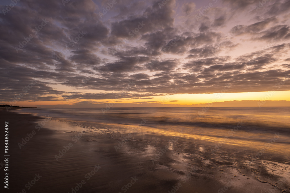 Obraz premium Sunrise at the beach with cloudy sky and smooth sand during morning hours